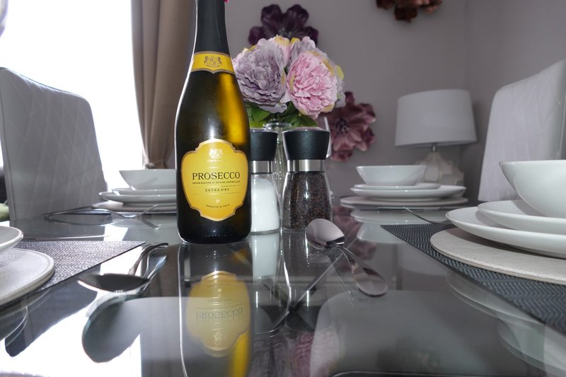 Dining table set with prosecco bottle, pink flowers, place settings and lamp