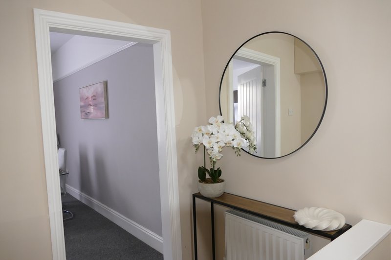 Hallway with round mirror, white orchid plant, and doorway to bedroom