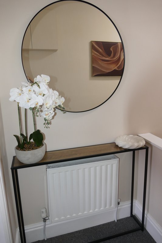 Entryway with round mirror, potted white orchids, black console table, and small framed art