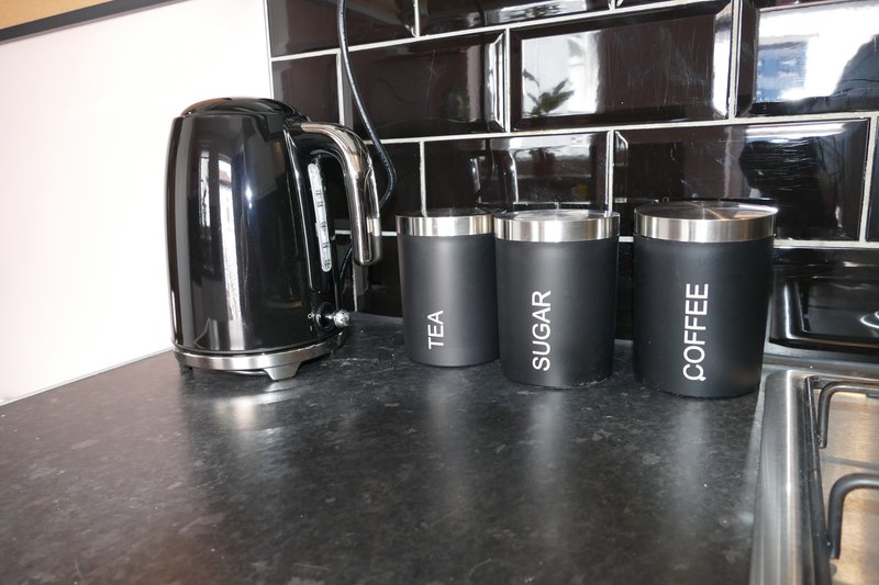 Kitchen counter with black kettle and labeled storage containers for tea, sugar, and coffee