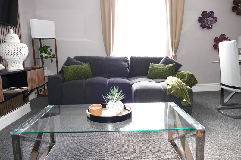 Modern living room with dark gray sofa, glass coffee table, green cushions and wall decor
