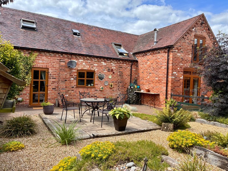Red brick cottage exterior with patio seating area and mature landscaped garden