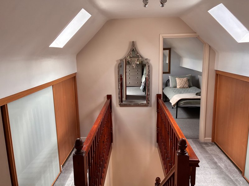 Attic hallway with wooden railings, skylights, and doorway to bedroom