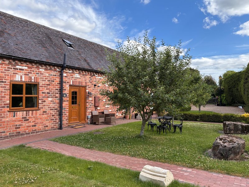 Brick cottage exterior with garden seating area, green lawn and mature trees