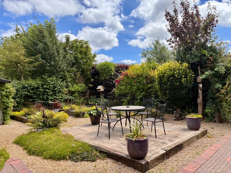 Outdoor patio with round table, chairs, and potted plants surrounded by mature trees