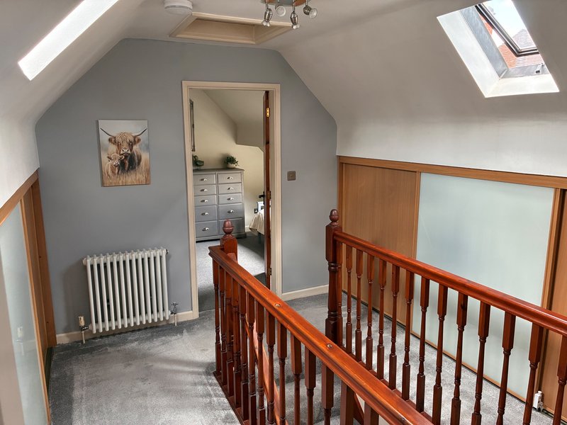 Bright attic landing with wooden staircase railing, gray walls, and open doorway to bedroom. Also featuring sliding wardrobe doors for clothes and hanging space