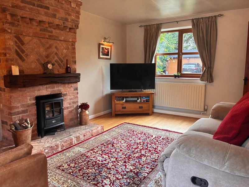 Living room with brick fireplace, wood stove, TV, reclining sofa with red cushion and patterned rug
