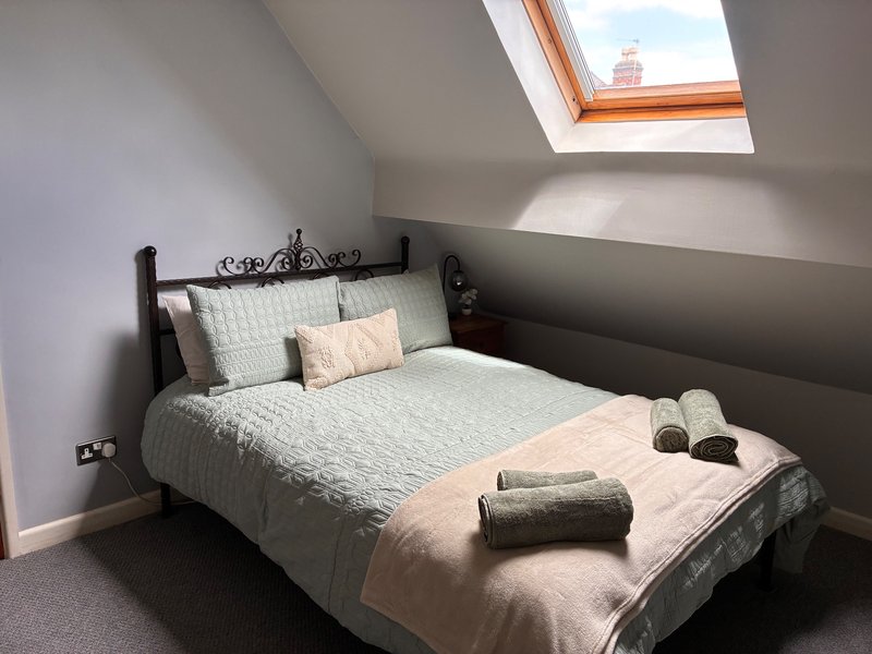 First bedroom - double bed, sage green bedding, skylight window and accent wall