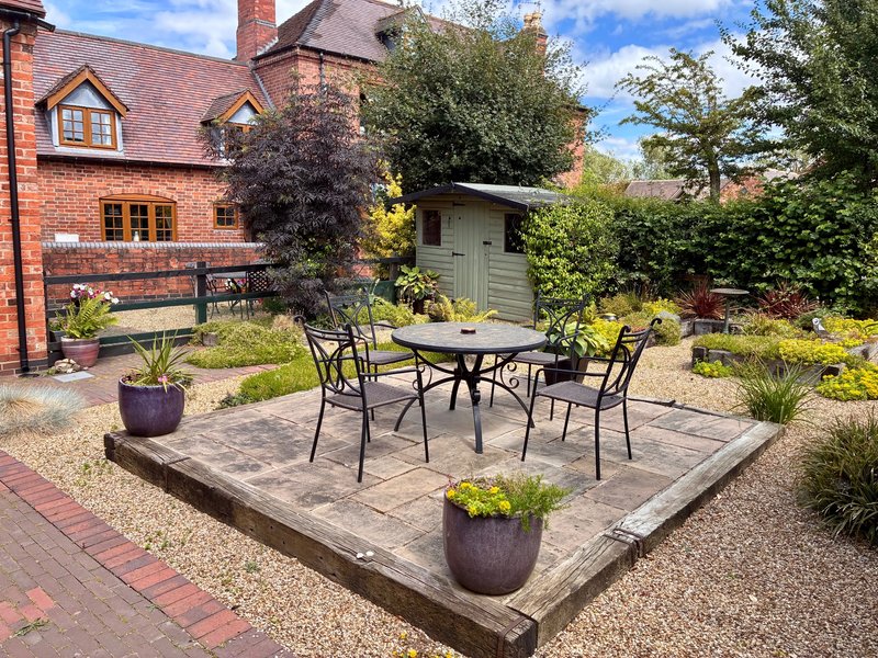 Brick cottage exterior with patio seating area, garden, and outbuildings
