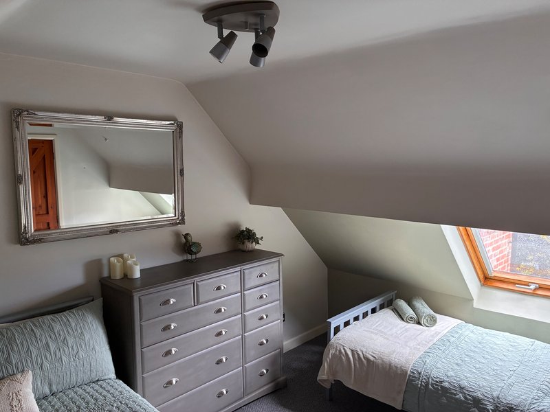 Second bedroom with two beds (double and single), chest of drawers, mirror, and skylight window