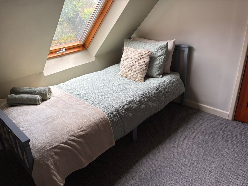 Bedroom 2 - Single bed with light bedding and pillows under sloped ceiling with skylight window