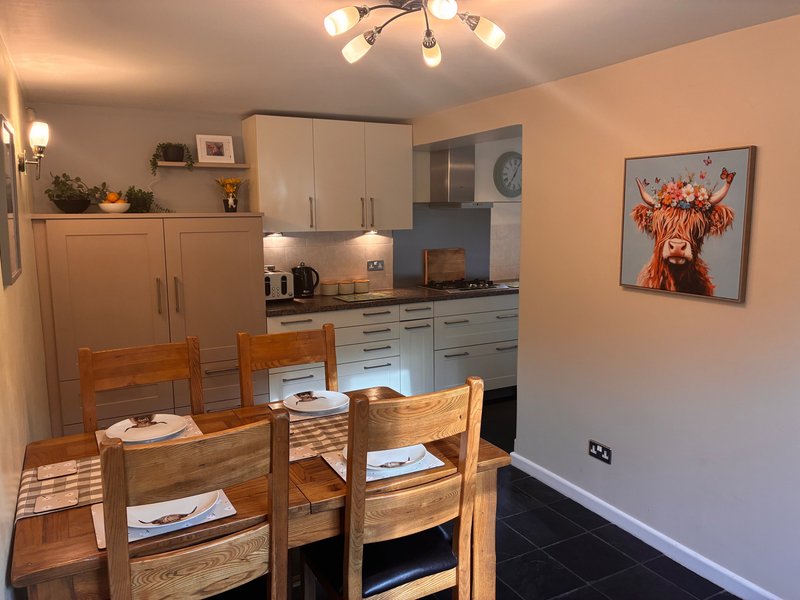 Open-plan kitchen and dining area with wooden table, cream cabinetry, and wall art