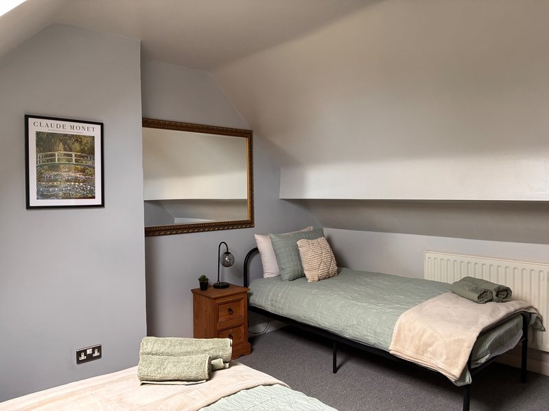 Modern bedroom with a double and a single bed, wooden nightstand, framed wall art, and radiator