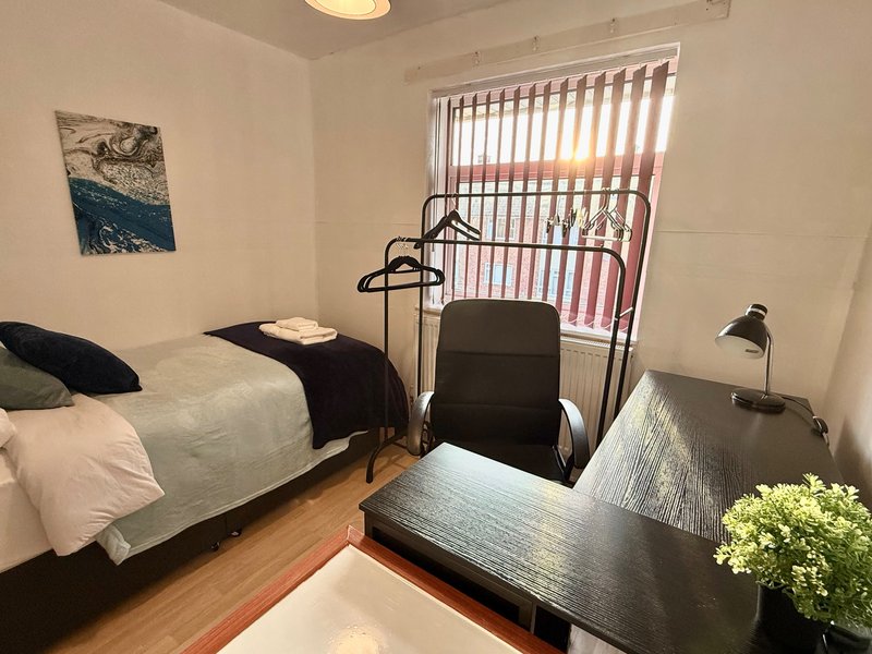 Bright bedroom with single bed, desk, chair, and window with vertical blinds