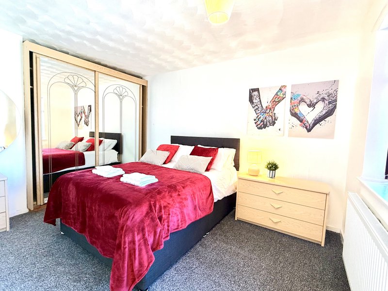 Bedroom with double bed, red velvet bedding, mirrored wardrobe and wooden chest of drawers