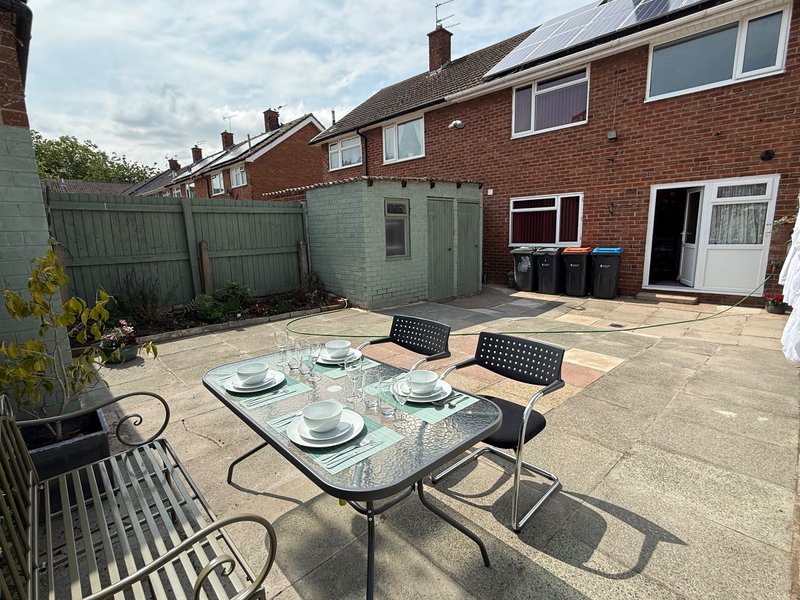 Paved garden patio with outdoor dining table, chairs, and brick semi-detached house