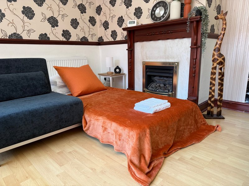 Living room with blue sofa, orange throw blanket, fireplace, and patterned wallpaper