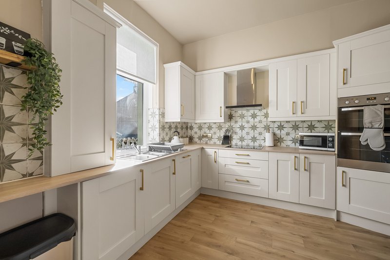 Modern kitchen with white cabinetry, geometric tile backsplash, wooden worktops and window view