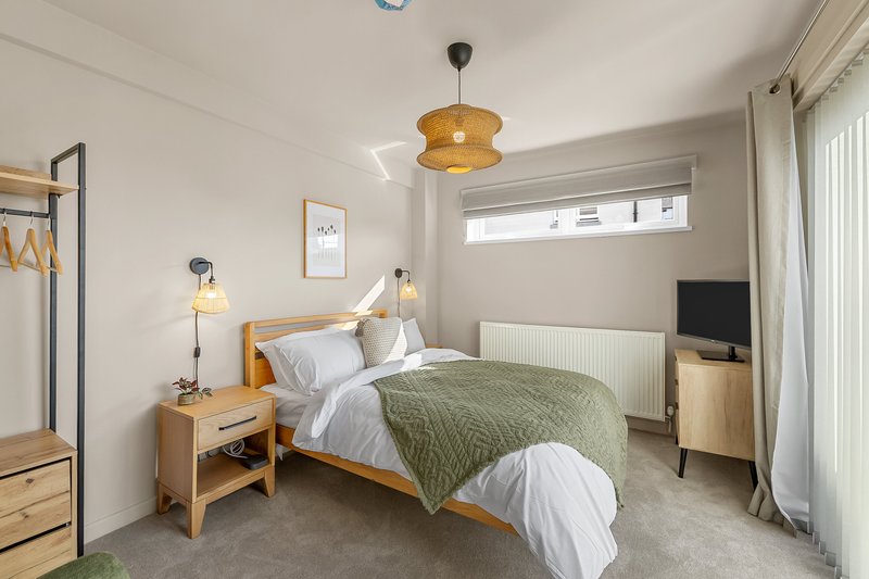 Bright modern bedroom with wooden bed frame, white bedding, green throw, pendant light and side table