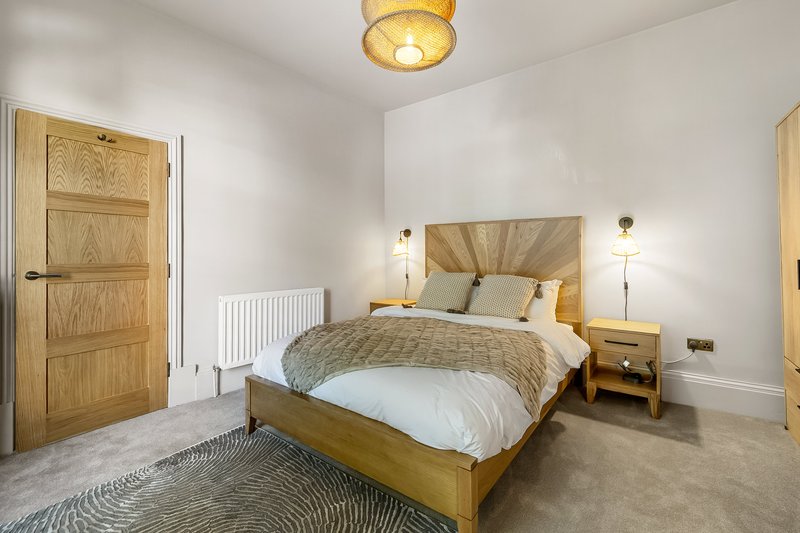 Bright bedroom with wooden bed, white bedding, gold headboard, wooden doors and pendant light