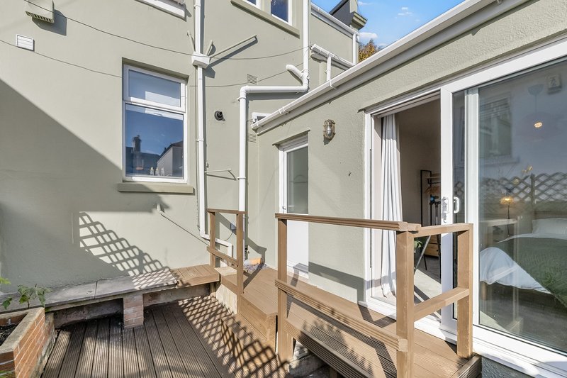 Wooden deck with railing overlooking garden, attached to modern cream-painted house with glass doors