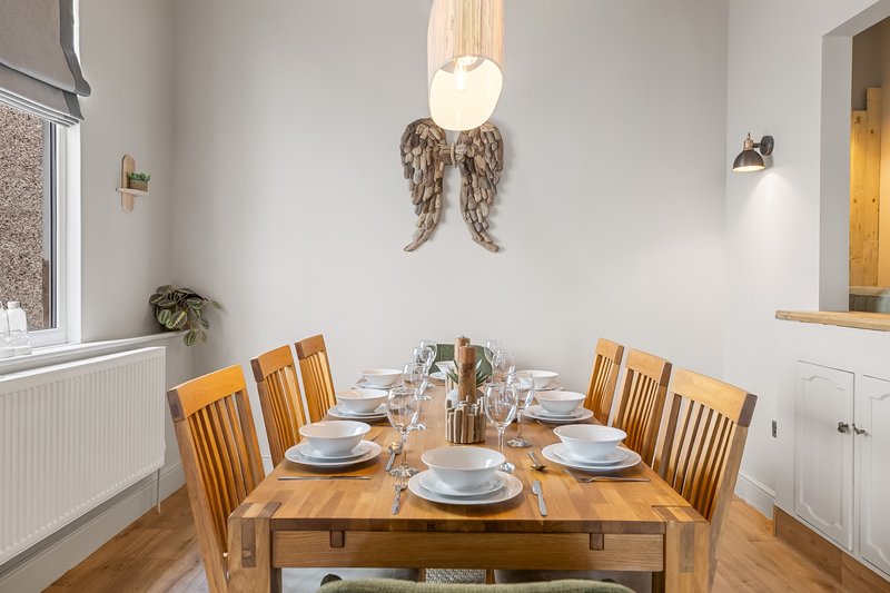 Dining room with wooden table, six chairs, place settings, and decorative wall hanging