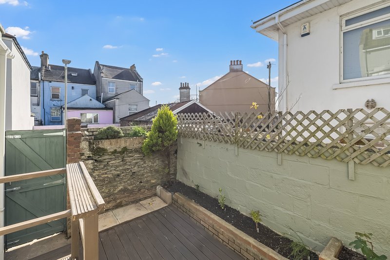 Rear garden with wooden decking, green fence, and neighbouring houses visible