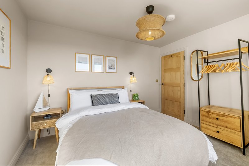 Bright modern bedroom with double bed, wooden nightstand, pendant lights, and clothing rack