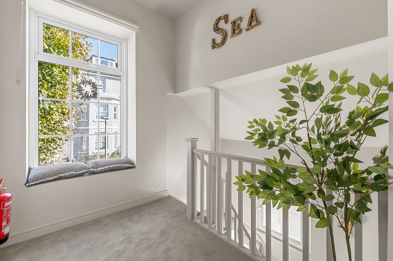 Bright stairwell with white railing, potted plant, window overlooking garden, sea-themed wall decor
