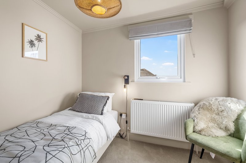 Bright bedroom with single bed, radiator, green armchair and woven ceiling light