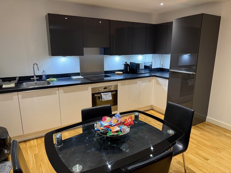 Modern kitchen with white and black cabinetry, blue splashback, and dining table with colorful fruit bowl