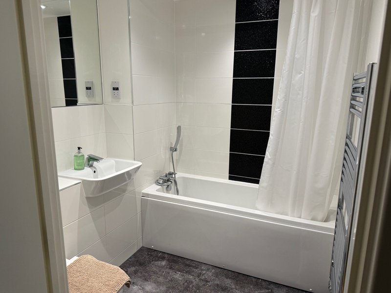Modern bathroom with white bathtub, wall-mounted sink, black and white tile walls, and shower curtain