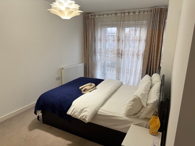 Bedroom with double bed, white pillows, blue and white bedding, pendant light fixture, and patio doors with curtains