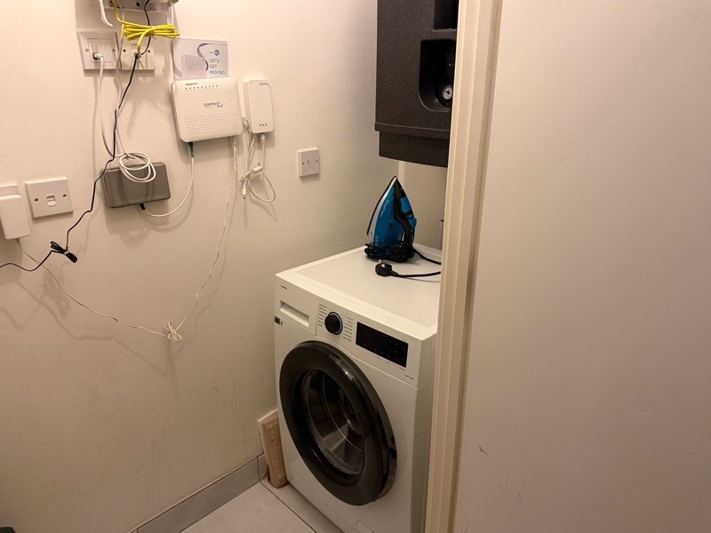Compact laundry room with washing machine, iron on top, and wall-mounted electrical outlets