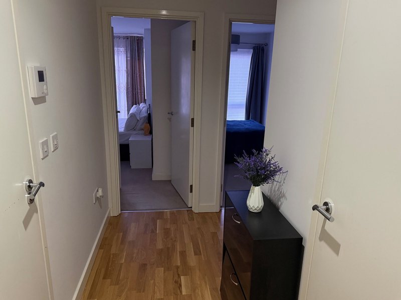 Hallway with wooden flooring, white walls, dark console table with flowers, and open doorways to adjacent rooms