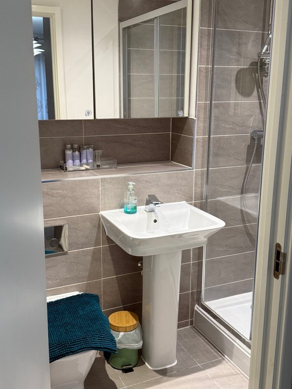 Modern bathroom with pedestal sink, shower enclosure, mirror and tiled walls