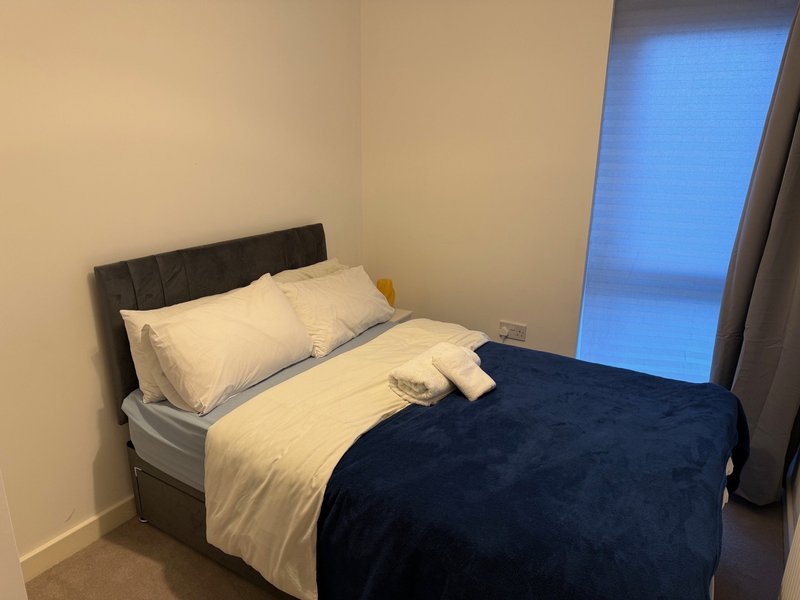 Modern bedroom with double bed, cream and navy bedding, black headboard, and blue window