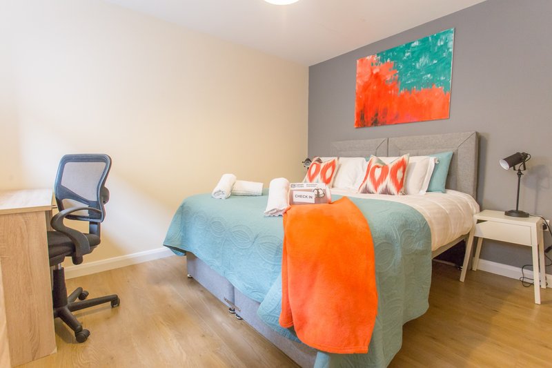 Bright bedroom with double bed, desk chair, abstract wall art and wooden flooring