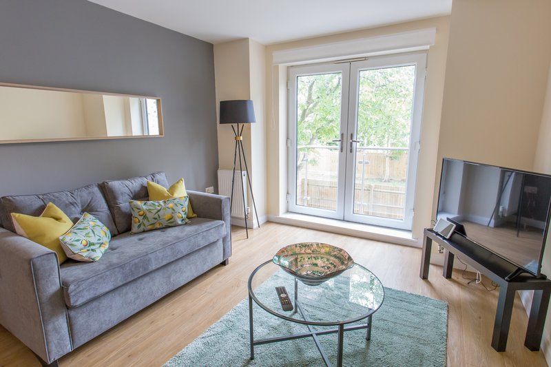 Modern living room with grey sofa, yellow cushions, glass coffee table and TV
