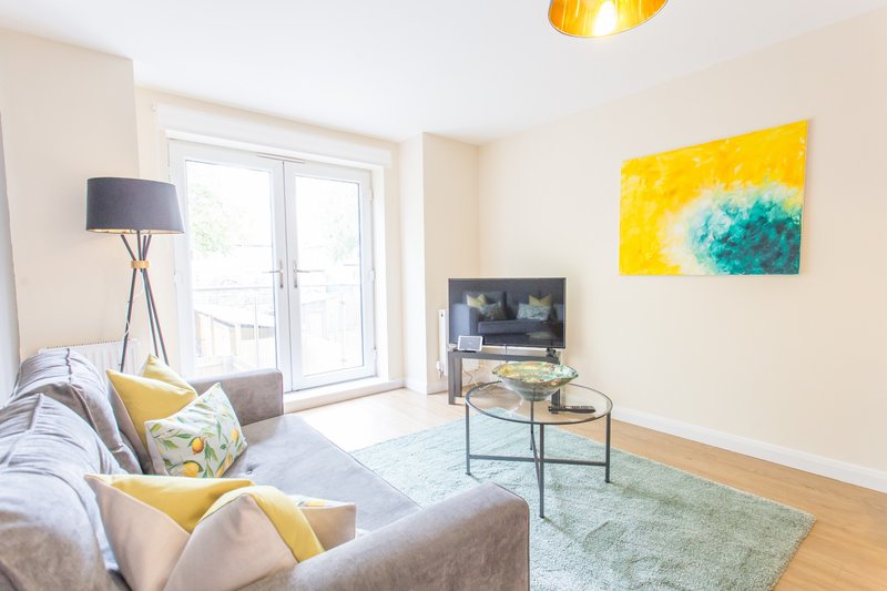 Bright living room with grey sofa, yellow cushions, wooden floor and glass doors
