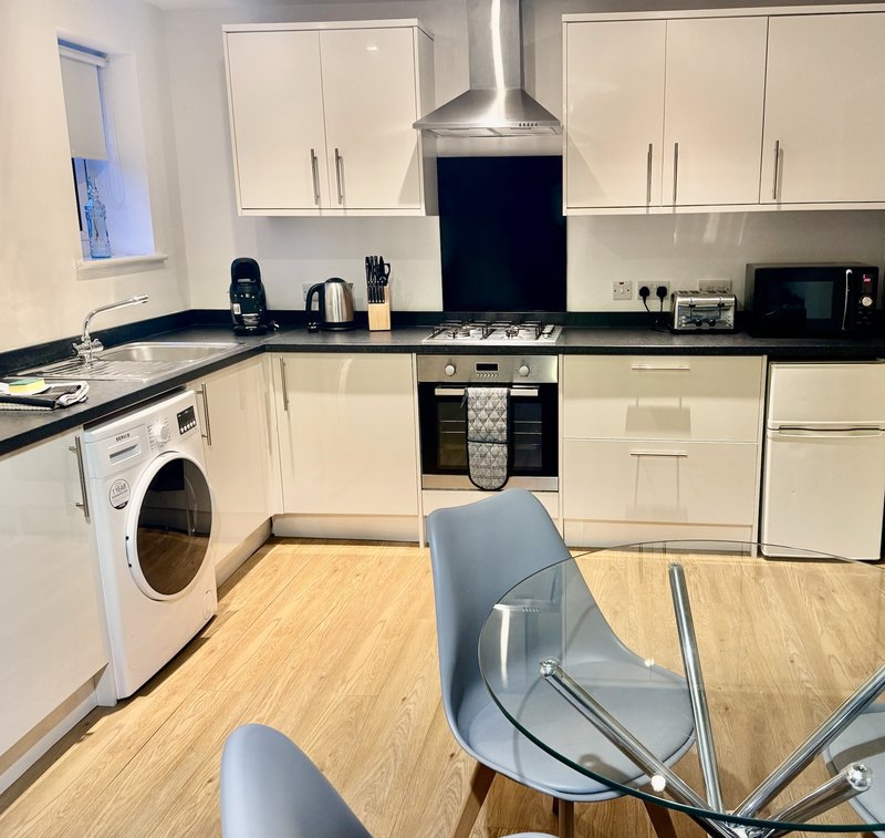 Modern kitchen with cream cabinets, black countertops, integrated appliances and wooden flooring