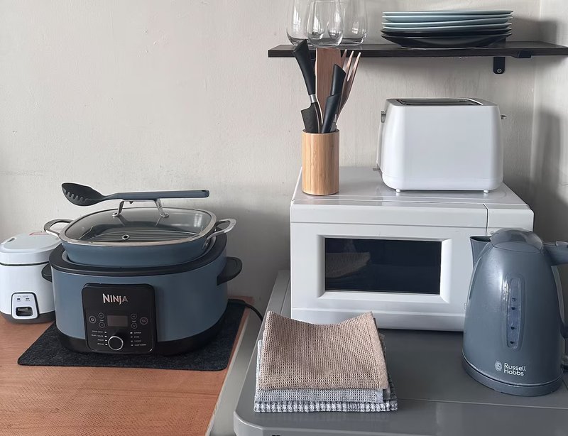 Kitchen counter with Ninja slow cooker, white microwave, kettle, utensils holder and shelving