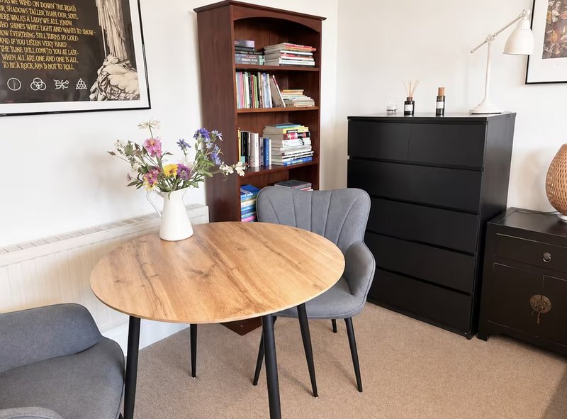 Dining room with round wooden table, grey chairs, bookshelf and black dresser