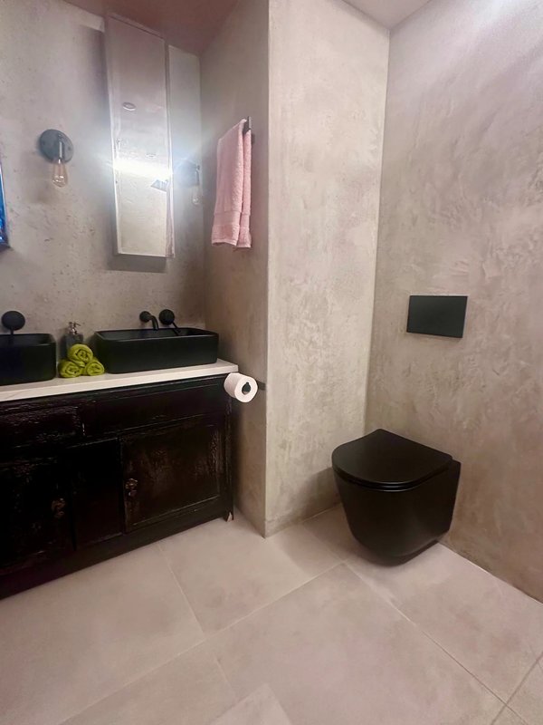 Modern bathroom with black toilet, dark vanity unit, mirror, and beige tiled walls