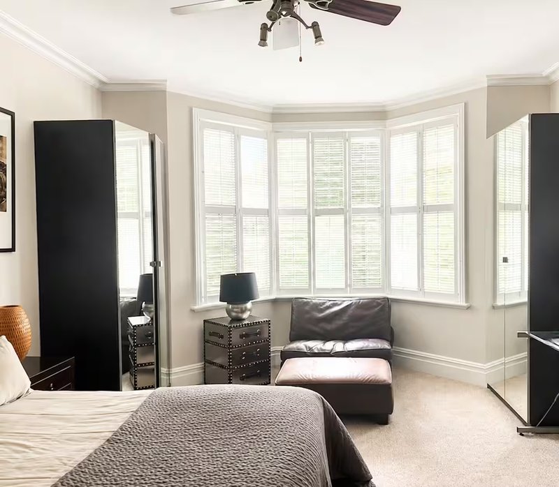 Bright bedroom with double bed, bay window seating area, ceiling fan and modern furnishings