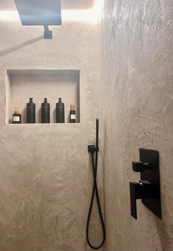 Modern bathroom shower alcove with dark toiletries bottles, black fixtures and skylight