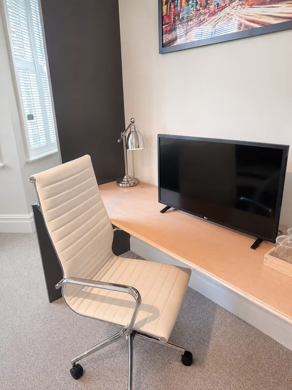 Home office with beige desk chair, wooden desk, monitor, and window with blinds