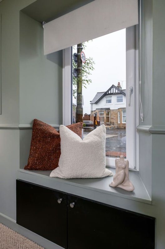 Window seat with cushions and decorative items, view of house and garden outside
