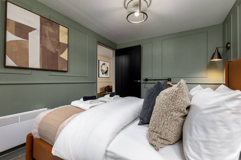 Modern bedroom with twin beds, green paneled walls, framed artwork and pendant lighting