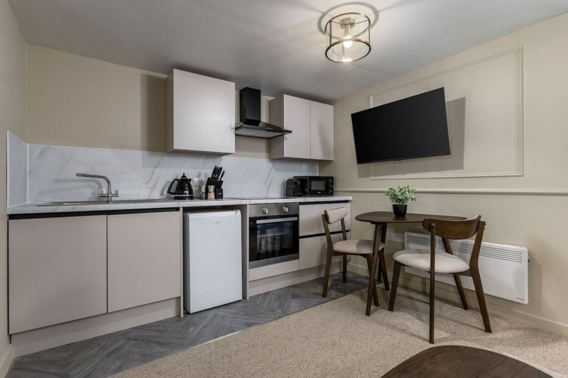 Modern kitchen with white cabinetry, marble backsplash, dining table and wall-mounted TV